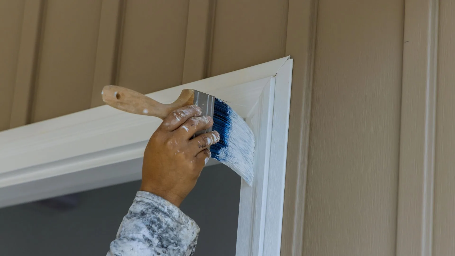 Brush painting exterior window trim on a wooden house