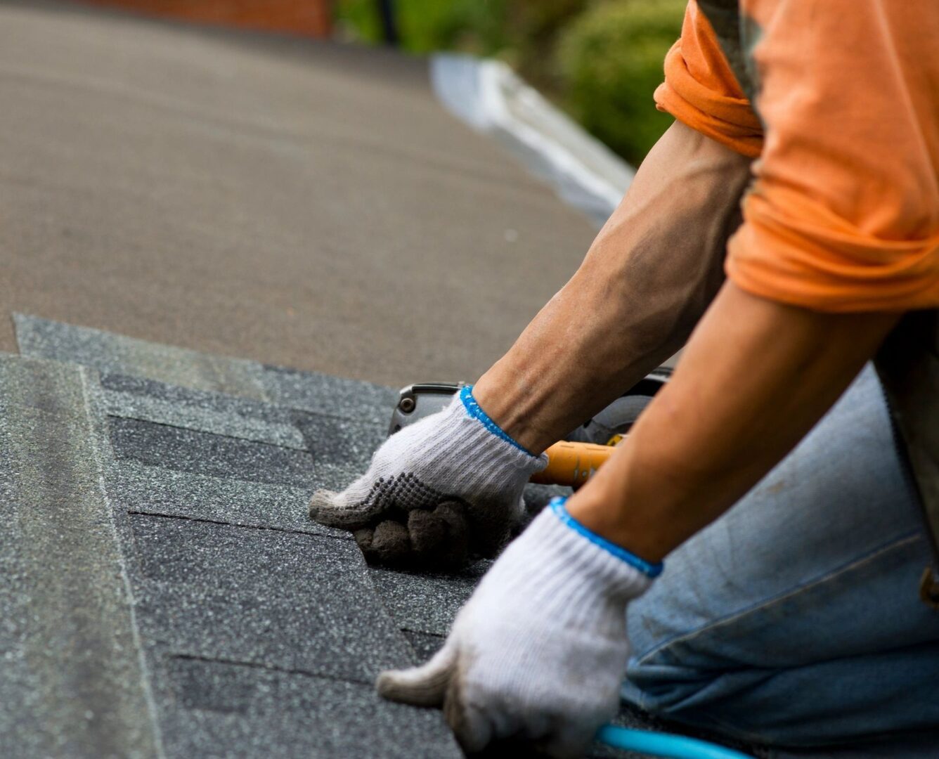 A person with gloves on working on the roof of a house.